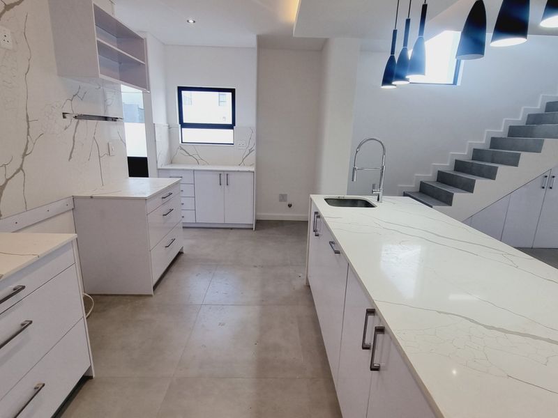 Modern kitchen featuring a large island with stone countertops, sleek white cabinetry, and integrated staircase access in a bright, open-plan layout.