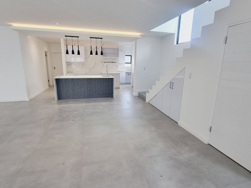 Modern open-plan living area featuring a sleek kitchen with a central island, under-stair storage, and neutral tiled flooring throughout.