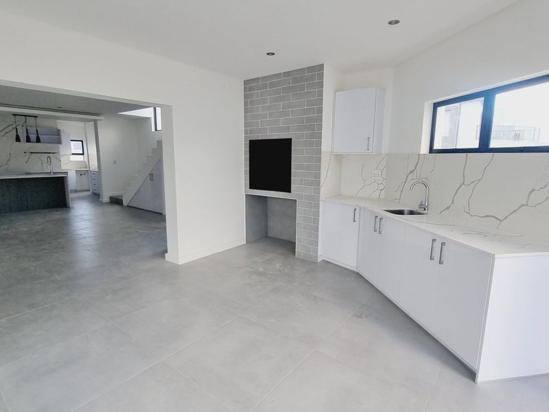 Modern open-plan living area featuring a built-in braai, sleek white cabinetry, stone countertops, and large format floor tiles.