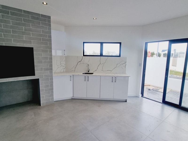 Modern open-plan living area featuring a grey brick fireplace, sleek white cabinetry with marble-look splashback, and large sliding doors leading to the exterior.