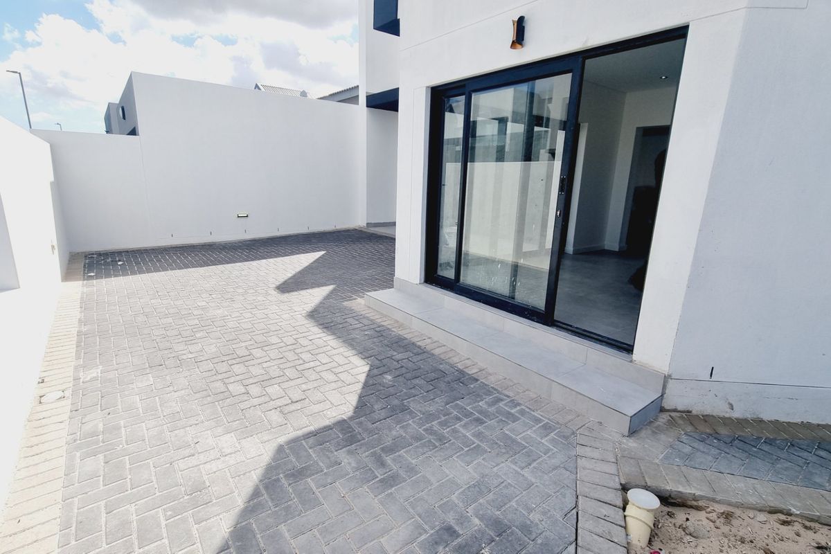 A modern rear exterior view featuring paved ground, a clean white facade, and a large sliding glass door providing access to the interior.