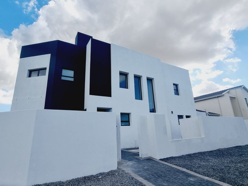A modern two-story residential facade featuring a striking black and white architectural design with clean lines and a paved entrance walkway.