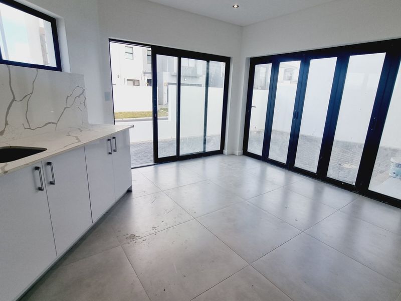 Modern open-plan kitchen area featuring stone countertops, marble-look splashback, and large glass doors providing seamless access to the outdoor space.