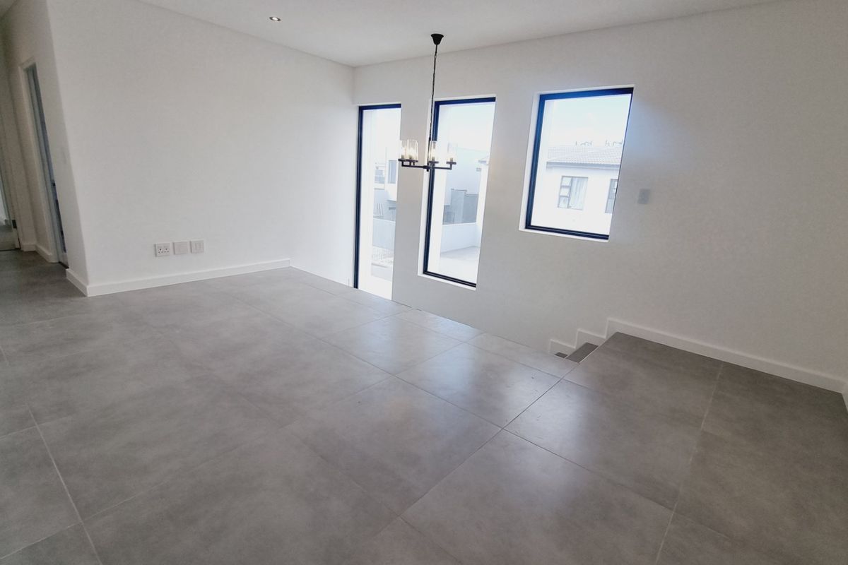 A bright, modern, and spacious living area featuring large windows, neutral tiled flooring, and recessed lighting, ready for personalization.