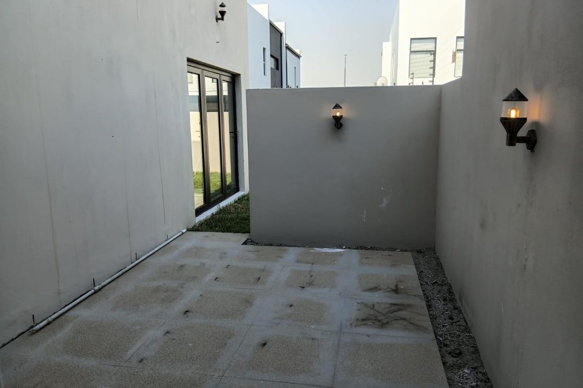 A compact rear patio area featuring paved flooring, wall-mounted lighting, and access to the interior via a sliding glass door.