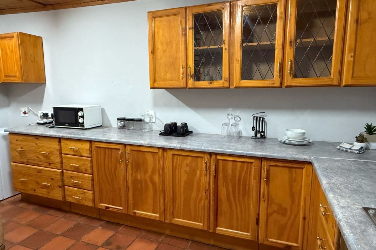 A functional kitchen featuring traditional wooden cabinetry, leaded glass display cupboards, durable laminate countertops, and classic terracotta floor tiles.