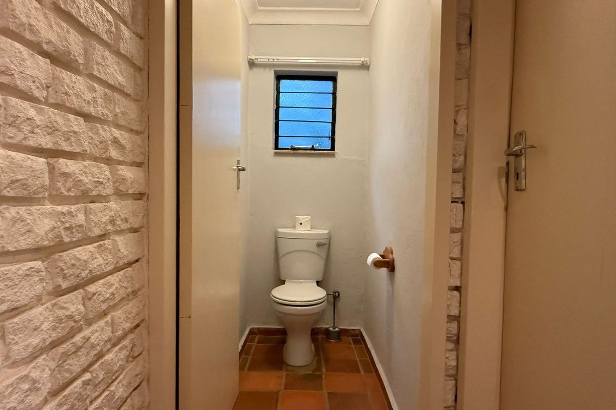 A compact guest bathroom featuring terracotta floor tiles, an exposed brick wall, and a standard toilet suite.