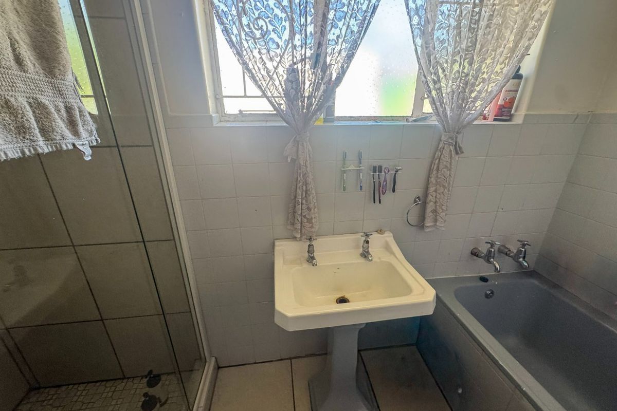 A functional bathroom featuring a pedestal basin, built-in bathtub, and a separate shower enclosure with tiled finishes throughout.