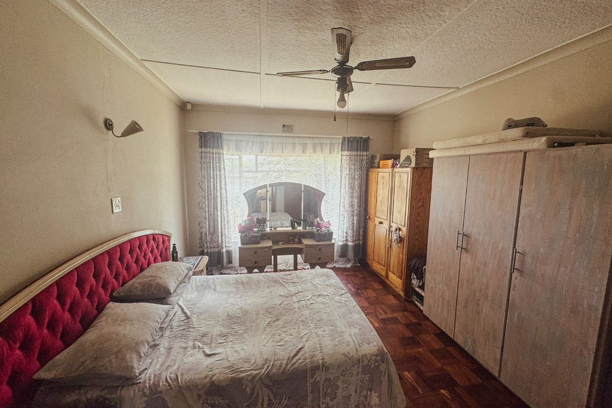 A bedroom featuring parquet flooring, a ceiling fan, and built-in cupboards. The room shows signs of wear and would benefit from cosmetic updates.