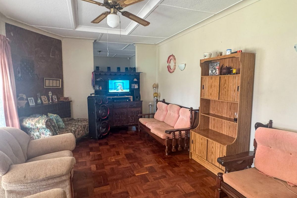 A living room featuring traditional parquet flooring, a ceiling fan, and coved ceiling details, offering a dated interior space ready for modernization.