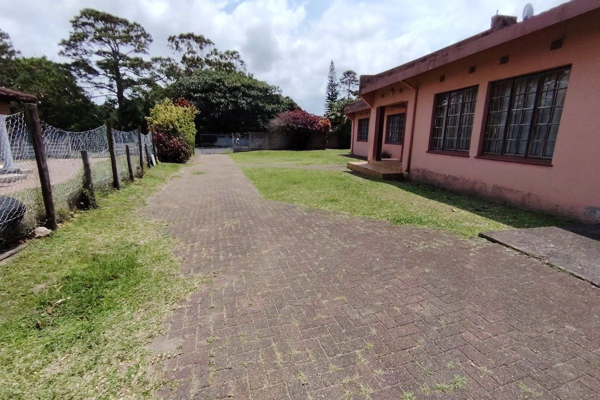 Rear exterior view of the property featuring a paved driveway, lawn area, and security fencing along the boundary.