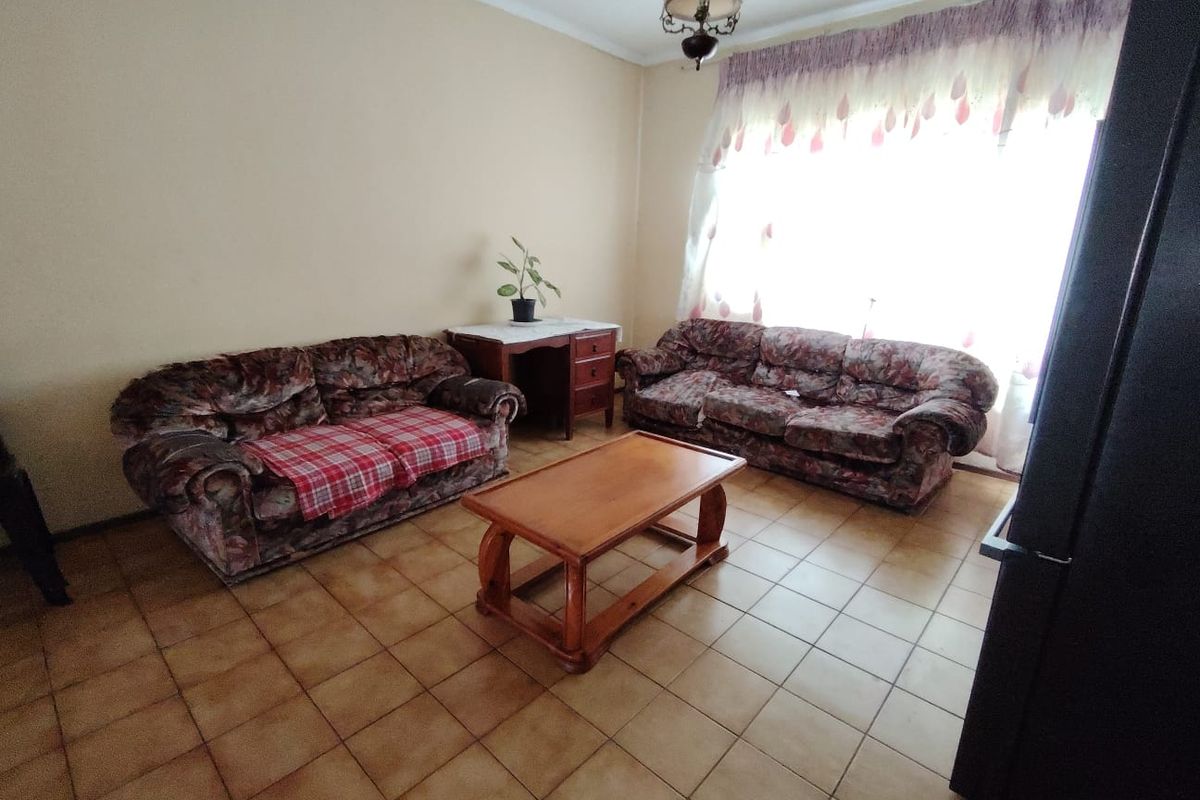 A living room featuring tiled flooring and a large window with natural light, providing a functional space ready for modern updates.
