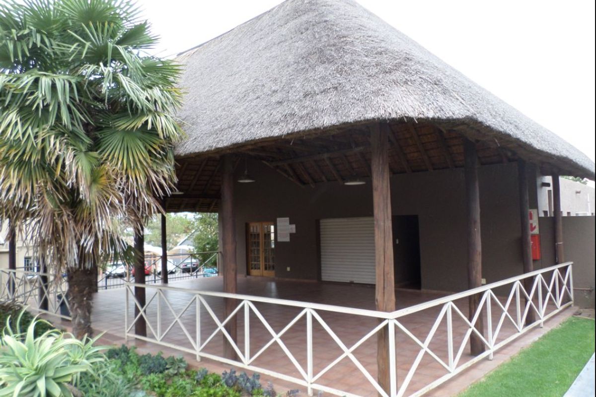 A covered outdoor clubhouse area featuring a traditional thatch roof, timber support columns, tiled flooring, and secure metal roller shutter access.