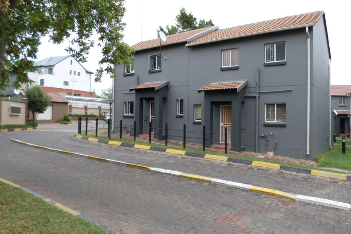 A view of the front facade of a two-story apartment complex featuring grey painted exterior walls, tiled roofing, and paved driveway access.