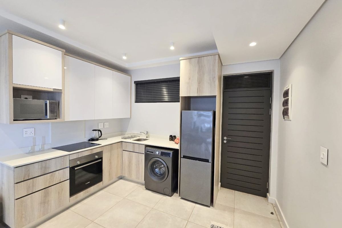Modern kitchen featuring light wood-grain cabinetry, white countertops, integrated appliances, electric hob, oven, and tiled flooring with recessed lighting.