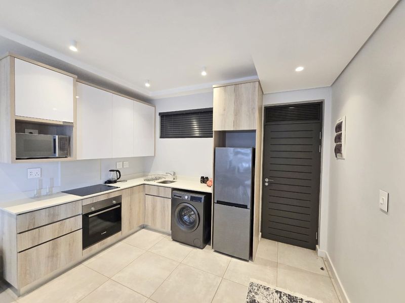 Modern kitchen featuring light wood-grain cabinetry, white countertops, integrated appliances, electric hob, oven, and tiled flooring with recessed lighting.