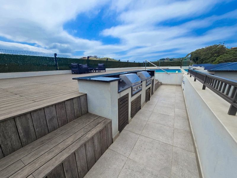 Spacious rooftop terrace featuring a built-in braai area with granite countertops, timber decking, and a private swimming pool with glass balustrades.