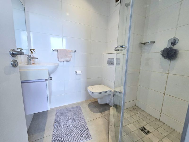 A functional bathroom featuring a wall-mounted toilet, a glass-enclosed shower, and a vanity basin with modern chrome fixtures.