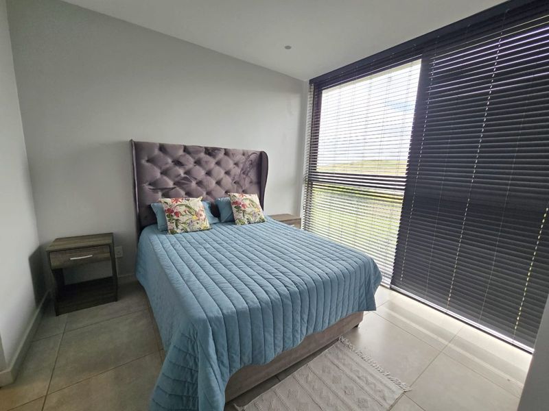 A modern bedroom featuring tiled flooring, recessed lighting, and a large sliding glass door with fitted venetian blinds, offering natural light and outdoor access.