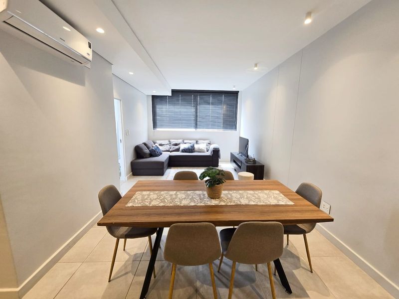 An open-plan living and dining area featuring tiled flooring, recessed downlighting, and a wall-mounted split-system air conditioner.