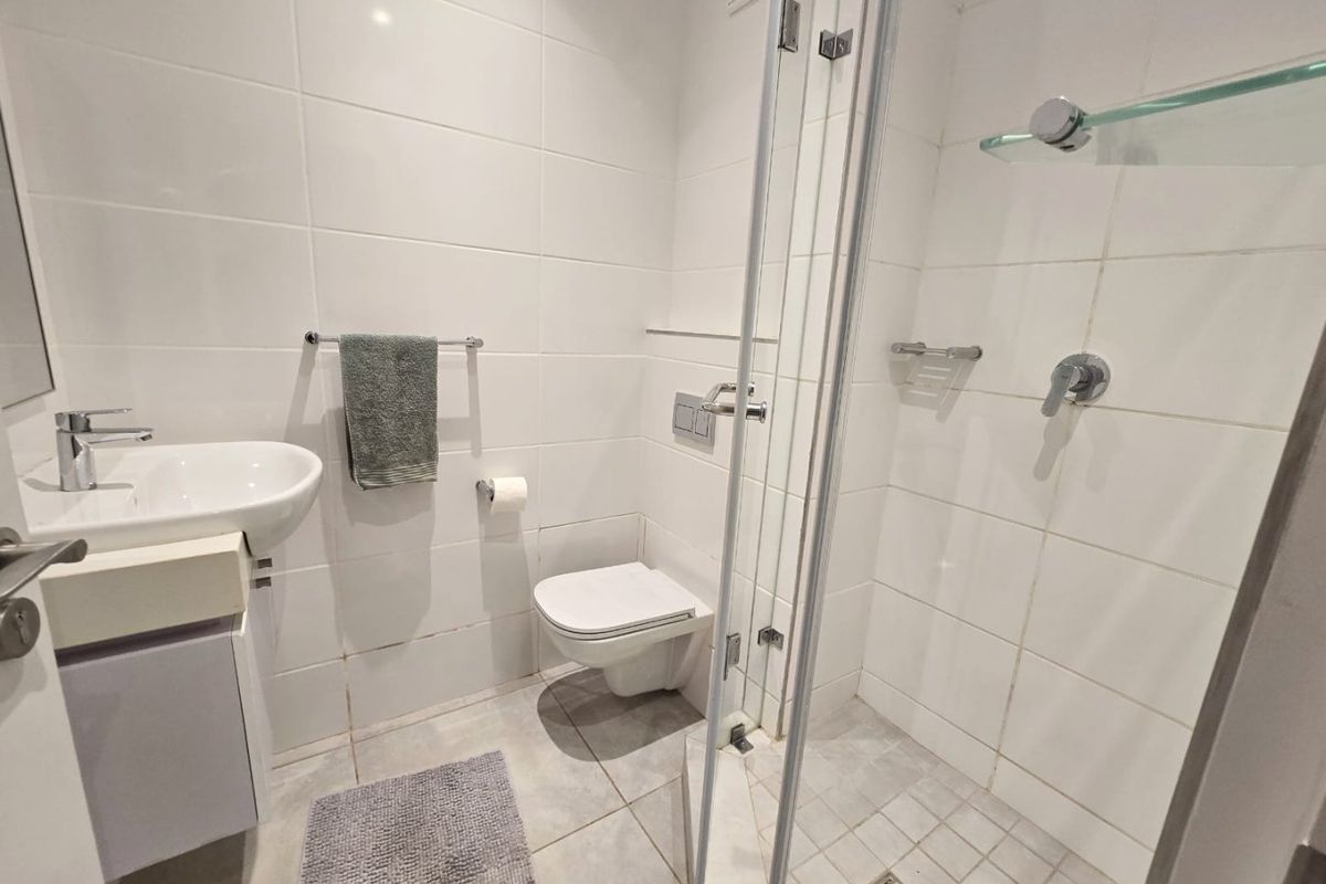 Compact modern bathroom featuring a wall-mounted toilet, vanity basin, and a glass-enclosed shower with white tiled finishes.