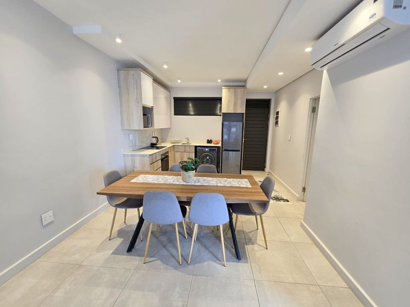 Modern open-plan kitchen and dining area featuring sleek built-in cabinetry, integrated appliances, tiled flooring, and a wall-mounted air conditioning unit.