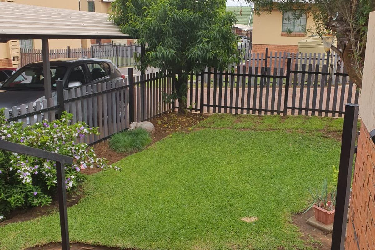 A private rear garden featuring a paved patio area, a well-maintained lawn, and a metal fence, with an adjacent carport structure.