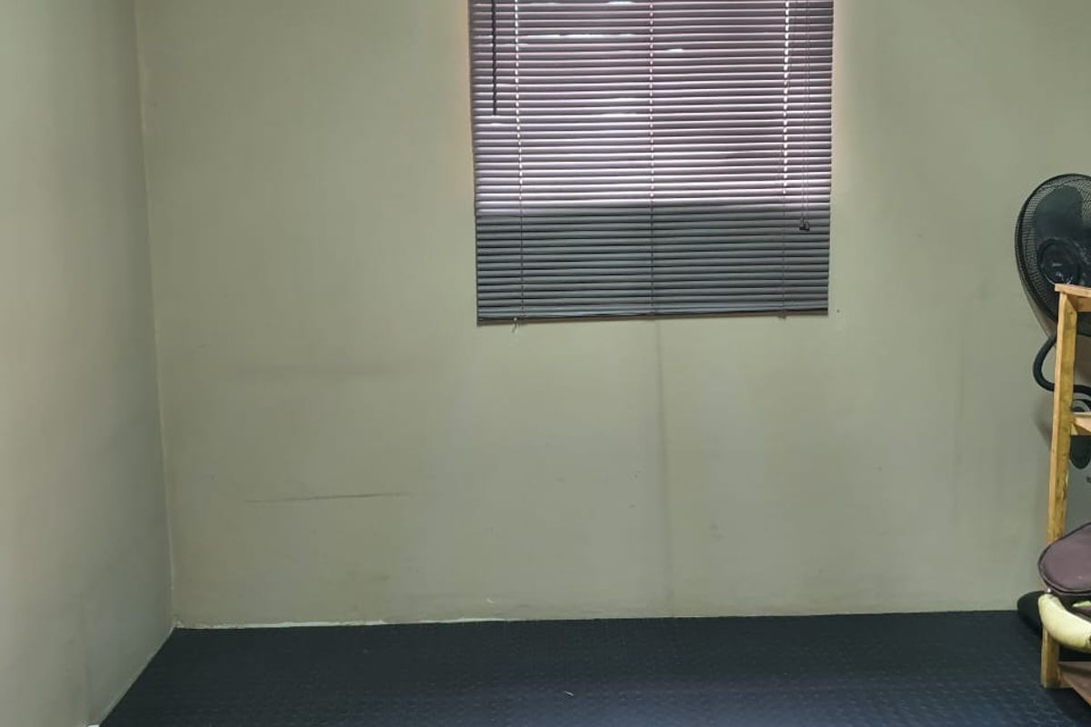 A sparsely furnished room featuring dark rubber flooring and a window fitted with venetian blinds, suitable for a bedroom or home office.