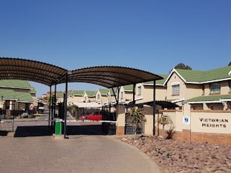 Entrance view of Victorian Heights townhouse complex featuring a security gate, covered carport, and paved driveway access.