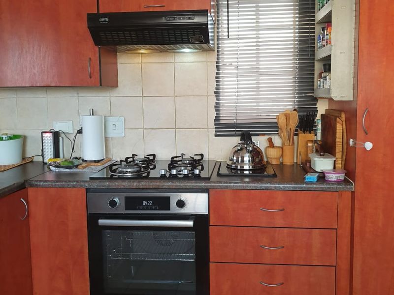 A functional kitchen featuring wood-finish cabinetry, a built-in gas hob, electric oven, extractor fan, and tiled backsplash with neutral floor tiles.
