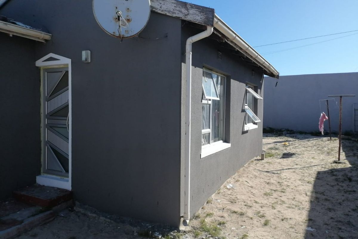 Rear exterior view of the house featuring grey painted walls, aluminium window frames, and a security door, with an unpaved yard area.