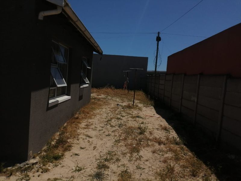A view of the rear exterior area featuring a precast concrete boundary wall and sandy ground space along the side of the house.