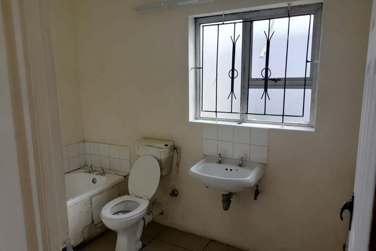 A dated bathroom featuring a bathtub, toilet, and wall-mounted basin, requiring renovation and cosmetic updates to improve its overall condition and appeal.