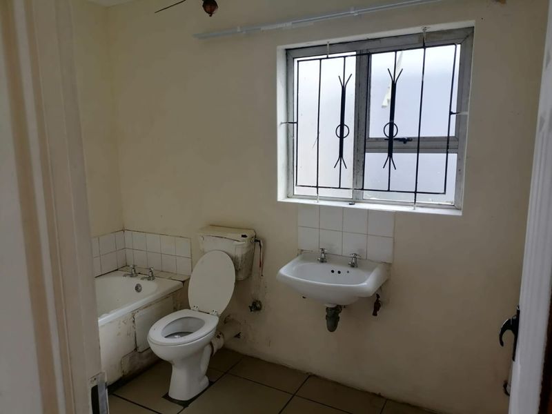 A dated bathroom featuring a bathtub, toilet, and wall-mounted basin, requiring renovation and cosmetic updates to improve its overall condition and appeal.
