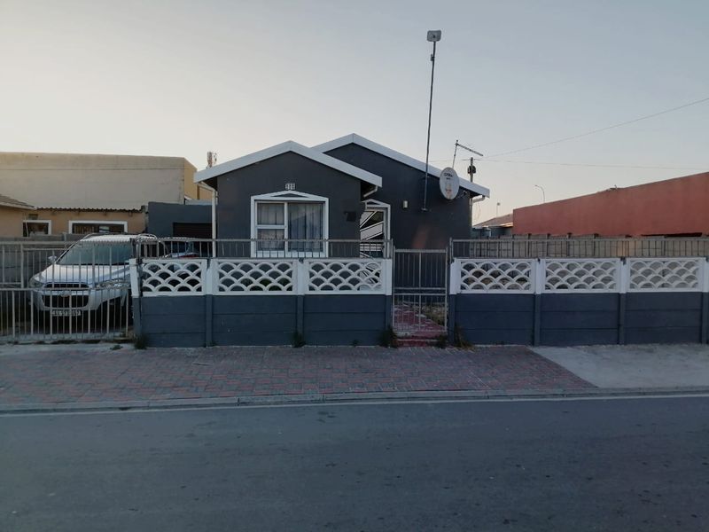 Front elevation of a detached house featuring a grey facade, secure precast concrete boundary wall, and a paved driveway entrance.