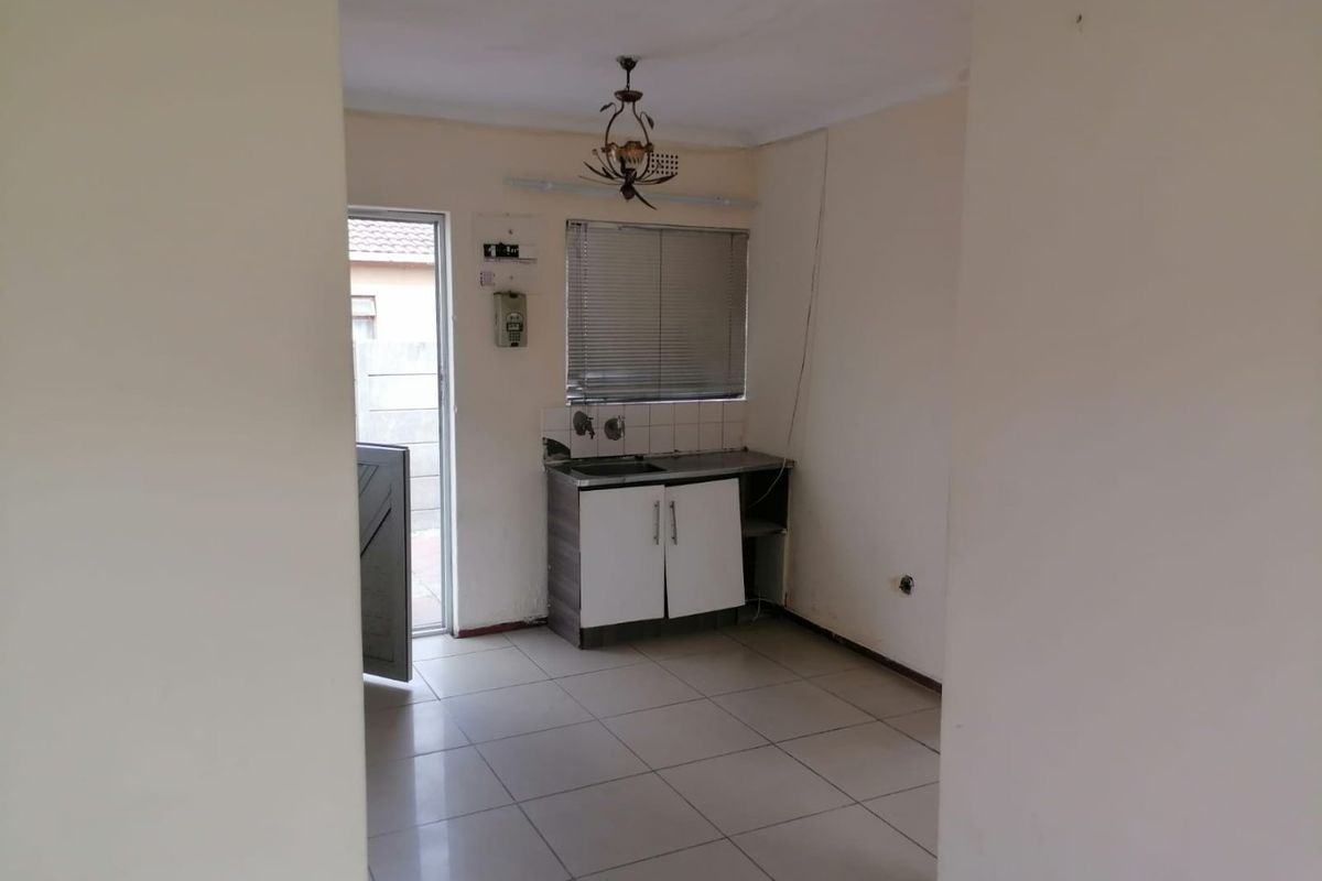 A compact, empty kitchen area featuring tiled floors, basic base cabinetry with a sink, and direct access to an exterior door.