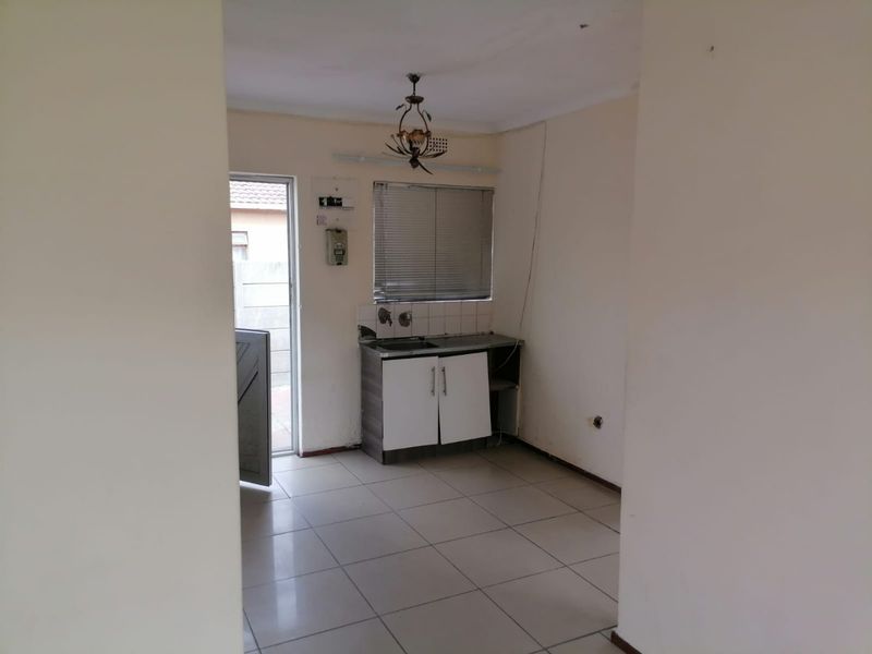A compact, empty kitchen area featuring tiled floors, basic base cabinetry with a sink, and direct access to an exterior door.