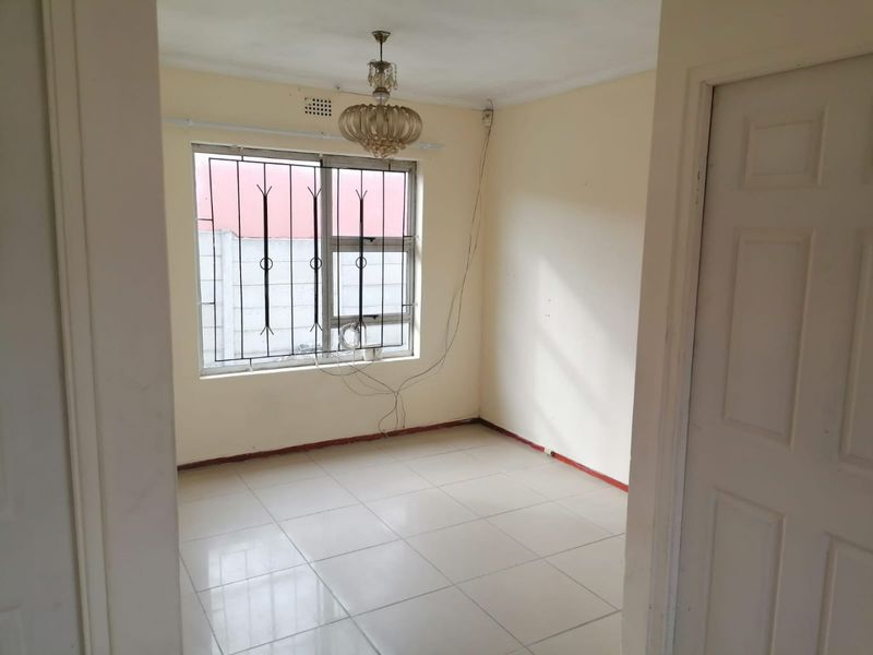 An empty bedroom featuring tiled flooring, security bars on the window, and a central light fixture, ready for a fresh update.