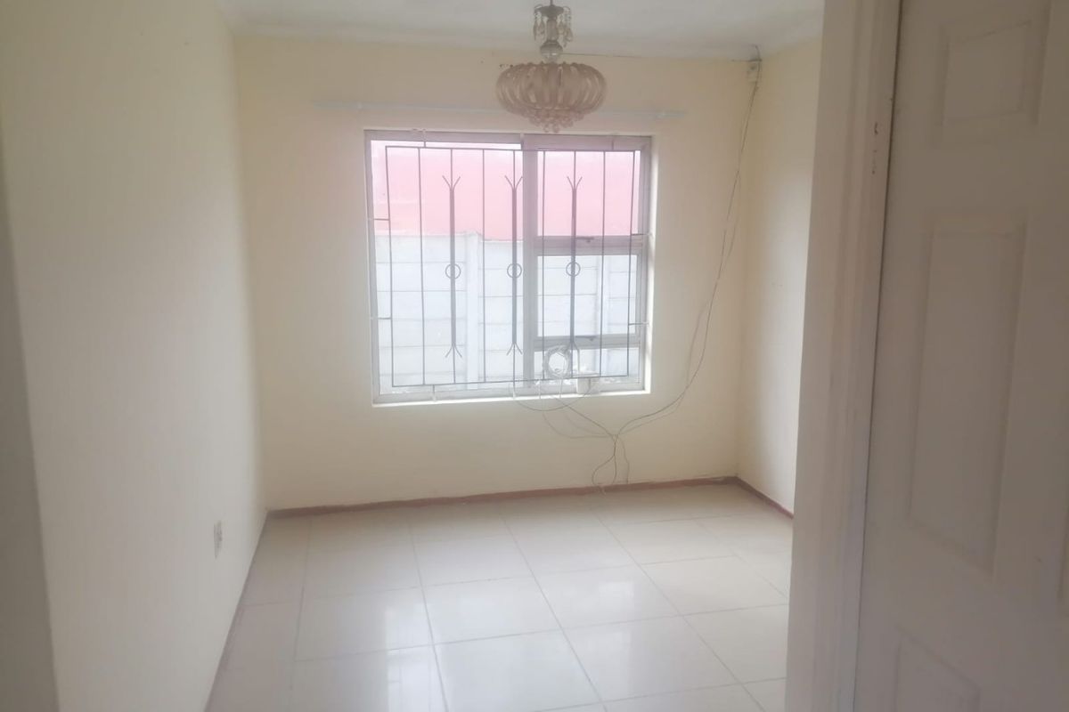 An empty bedroom featuring tiled flooring, a window with security bars, and a central ceiling light fixture.