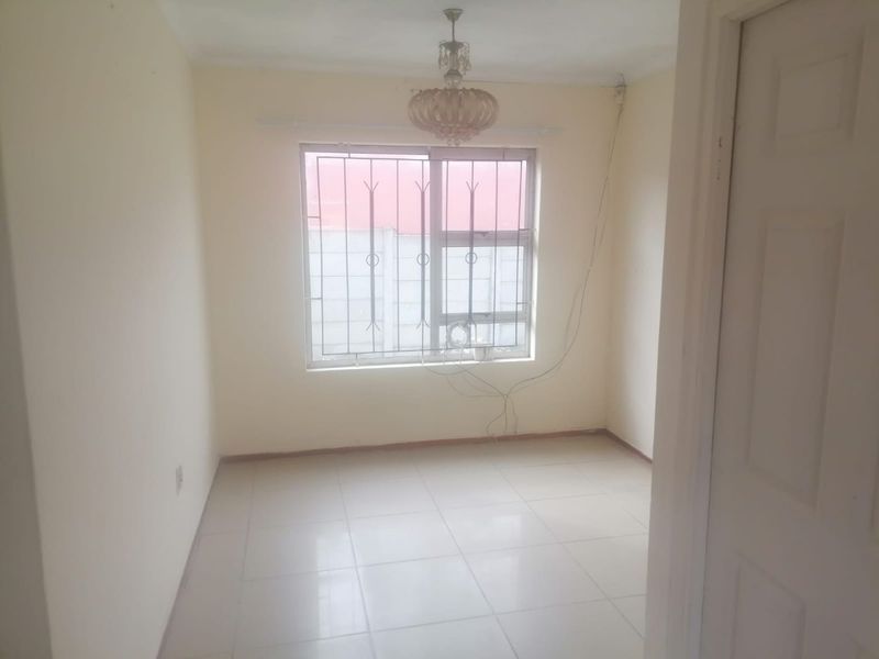 An empty bedroom featuring tiled flooring, a window with security bars, and a central ceiling light fixture.