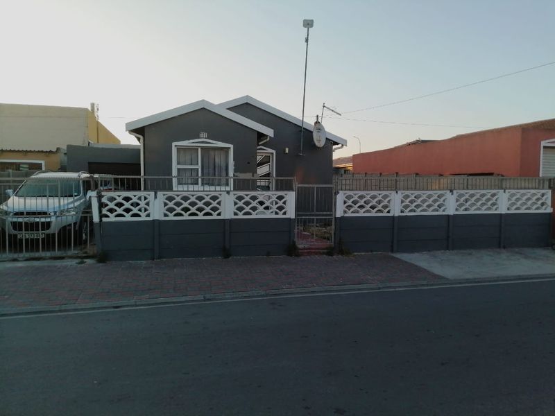 Front elevation of a single-story house featuring a gabled roof, paved driveway, and a secure precast concrete boundary wall with a metal gate.
