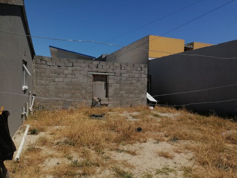 Rear exterior area featuring an unfinished concrete block wall, exposed plumbing, and an unmaintained yard space requiring landscaping and structural finishing.
