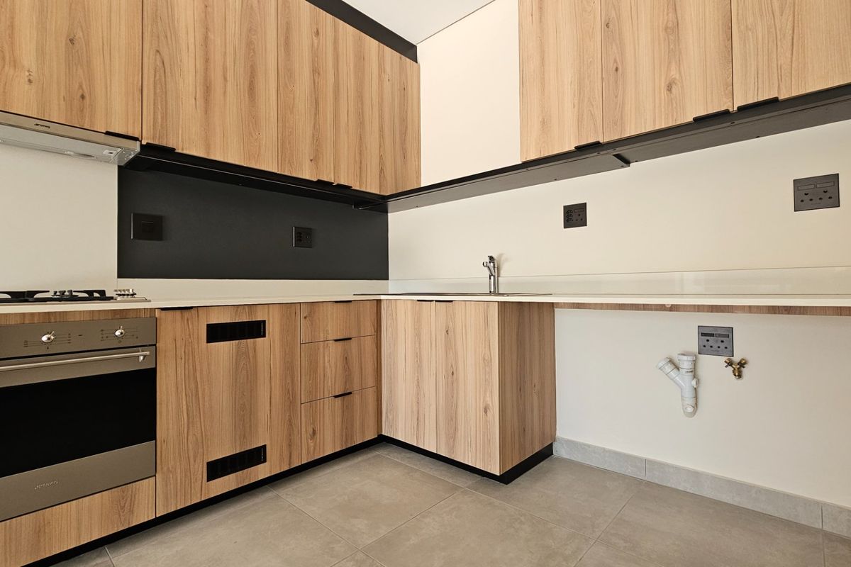 Modern kitchen featuring wood-look cabinetry, stone countertops, built-in oven, gas hob, and dedicated plumbing connections for appliances.