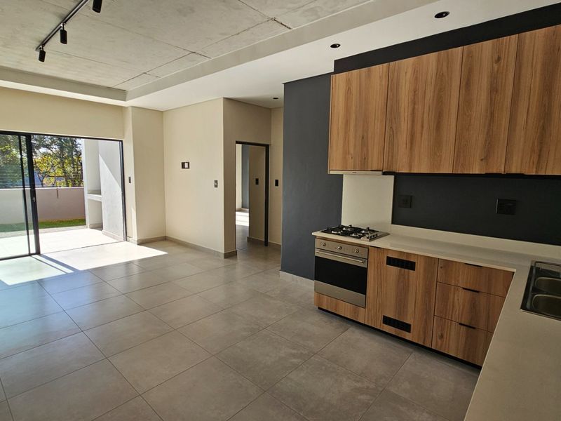 Modern open-plan kitchen and living area featuring sleek wood-finish cabinetry, stone countertops, integrated appliances, and seamless access to a private patio through sliding doors.