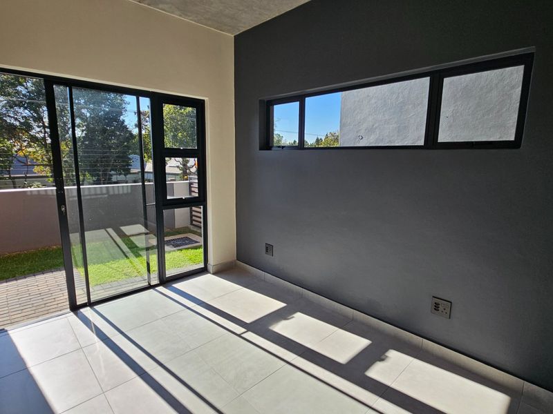 A bright, modern bedroom featuring large sliding glass doors leading to a patio, tiled floors, and a contemporary dark accent wall.