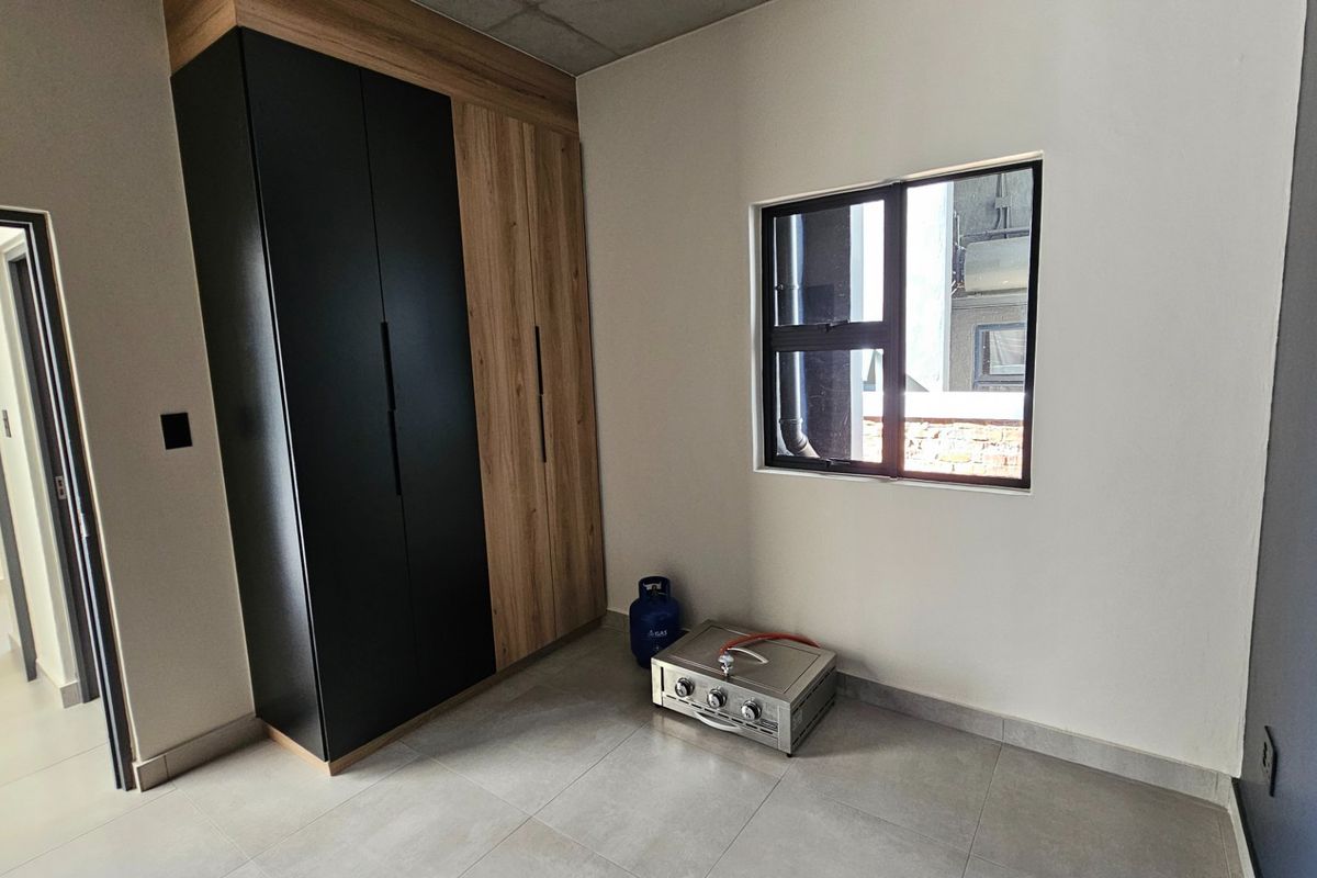 A modern, empty bedroom featuring sleek two-tone built-in cupboards, neutral tiled flooring, and a large window providing natural light.
