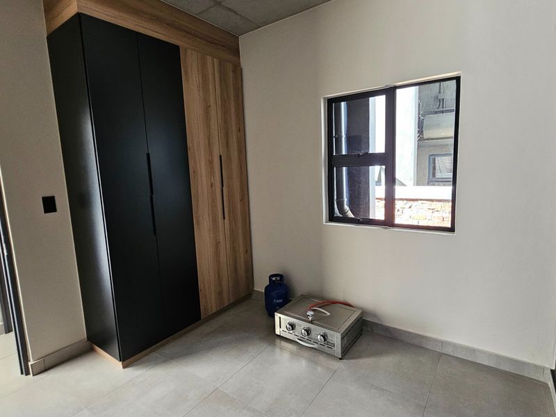 A modern, empty bedroom featuring sleek two-tone built-in cupboards, neutral tiled flooring, and a large window providing natural light.