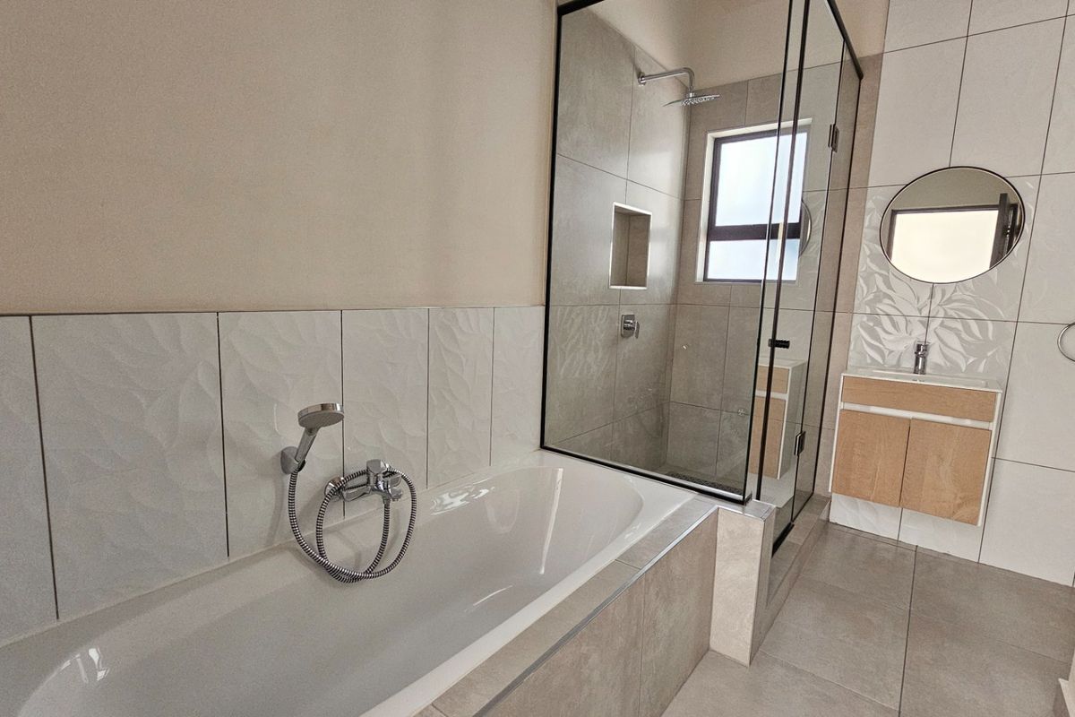 Modern bathroom featuring a bathtub, separate glass-enclosed shower, vanity cabinet with basin, and contemporary wall and floor tiling.