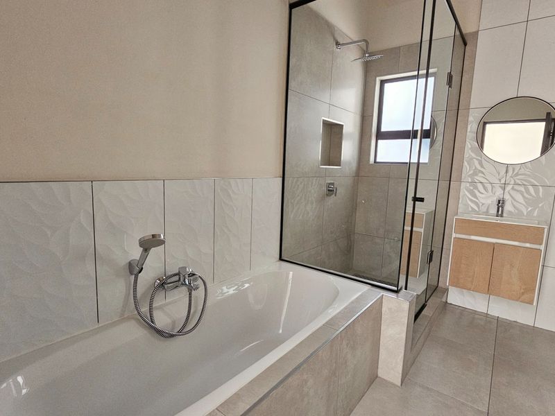 Modern bathroom featuring a bathtub, separate glass-enclosed shower, vanity cabinet with basin, and contemporary wall and floor tiling.