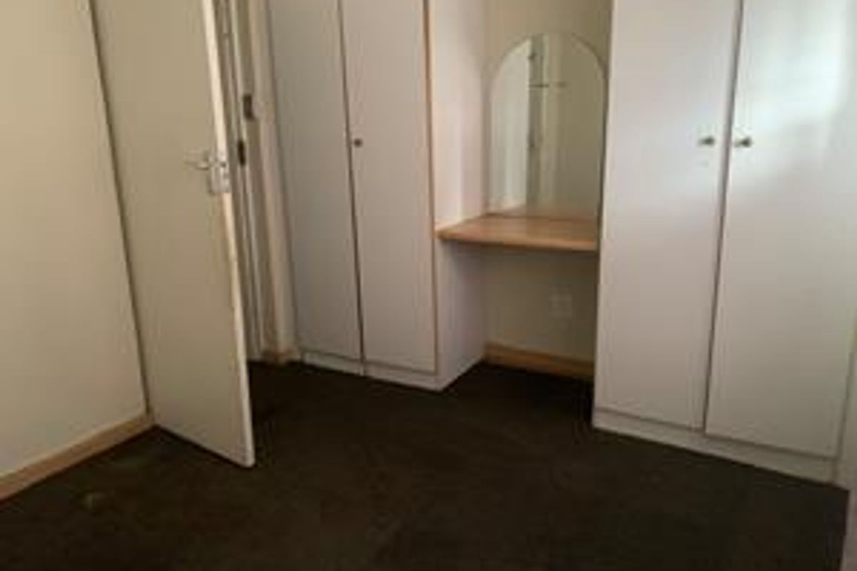 Bedroom featuring built-in cupboards and a integrated vanity station with a mirror, requiring cosmetic updates to flooring and finishes.